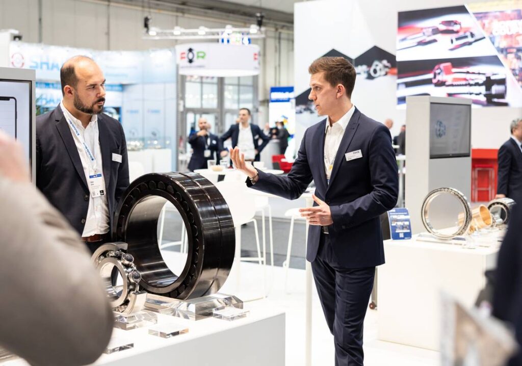 Two men on trade show floor conversing in front of large all black bearing